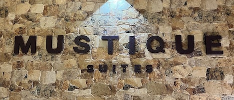 A stone wall with the words "MUSTIQUE SUITES" and a bottle silhouette.
