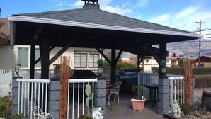 A covered patio area with a grill, seating, and decorative plants. - Mount View Motel (Oliver)