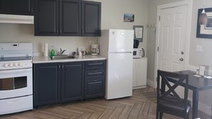 A kitchen with dark cabinets, a white refrigerator, a stove, and a dining area with a table and chair. - Mount View Motel (Oliver)