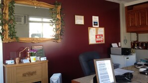 A room with a large ornate mirror, a desk with a computer and papers, a chair, and a small refrigerator. - Mount View Motel (Oliver)