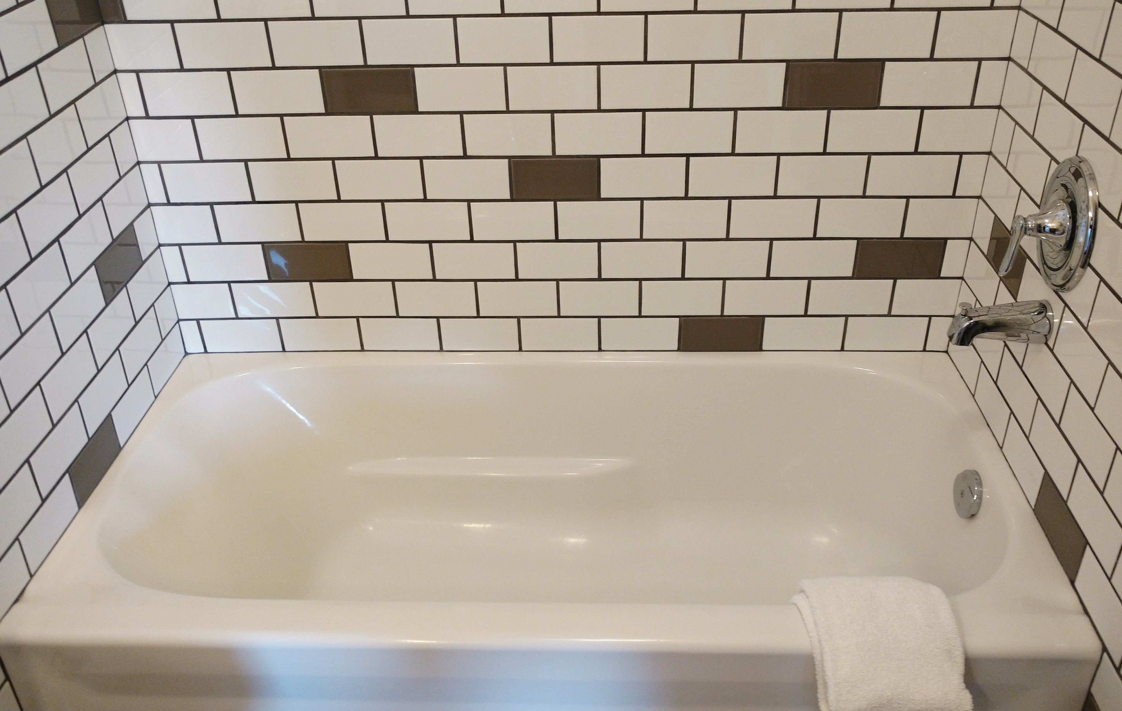 A bathtub with a white tile wall and a brown and white tile pattern.