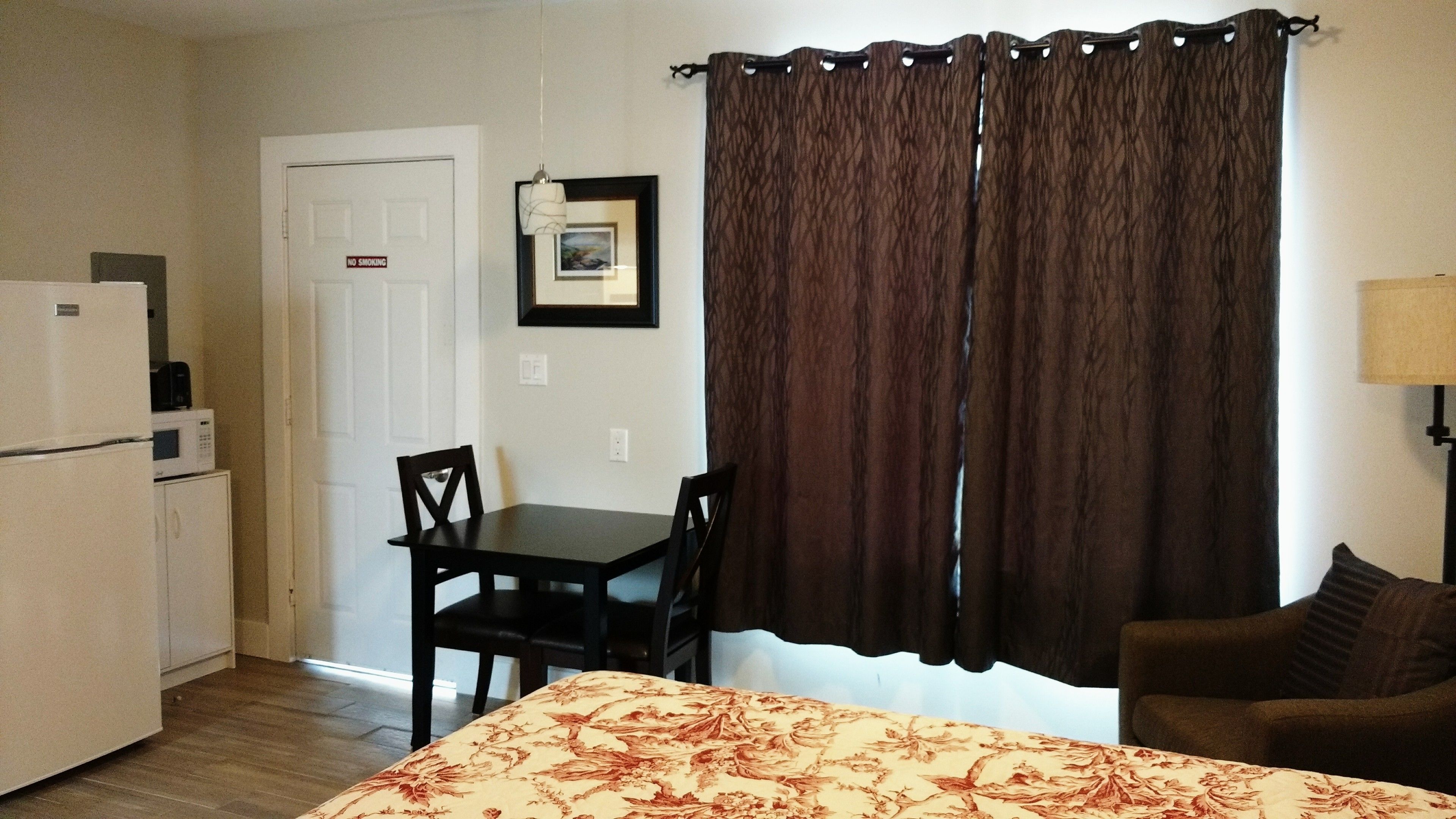 A compact room with a bed, a dining table with two chairs, a microwave, and a refrigerator.