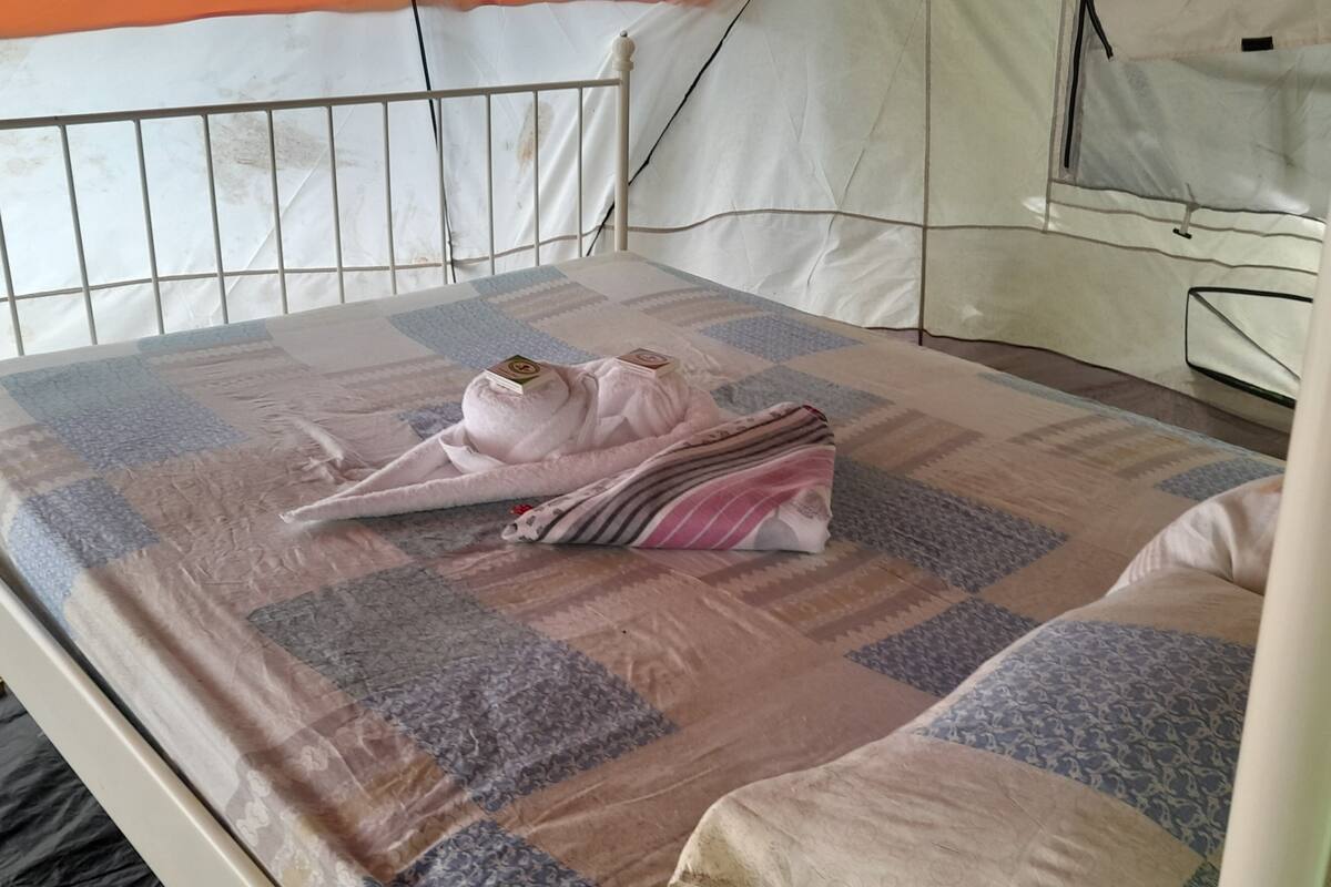 Ein Bett mit einer gesteppten Decke, einem weißen Metall-Kopfteil und einer weißen Wand.