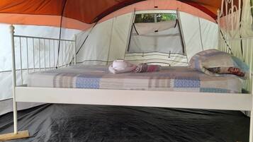 A bed with a metal frame, a mattress, and pillows inside a tent.