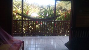 Un balcon avec un hamac, un sol carrelé et une vue sur une végétation tropicale.
