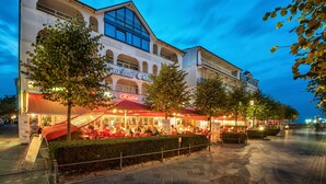 A restaurant with outdoor seating, a modern building with arched windows, and a clear sky. - Aparthotel Rialto & Hotel Esplanade (Binz)