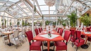 A restaurant with a glass ceiling, red and white chairs, and a central table with a menu. - Aparthotel Rialto & Hotel Esplanade (Binz)