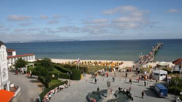 Ein öffentlicher Platz mit einem zentralen Brunnen, einer Uferpromenade und im Hintergrund Meer und Gebäude.