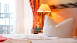 A hotel room with a neatly made bed, a bedside lamp, and a view of the outside. - Aparthotel Rialto & Hotel Esplanade (Binz)