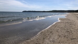 A beach with a sandy shore and calm water, a distant forested island, and a clear sky. - Aparthotel Rialto & Hotel Esplanade (Binz)