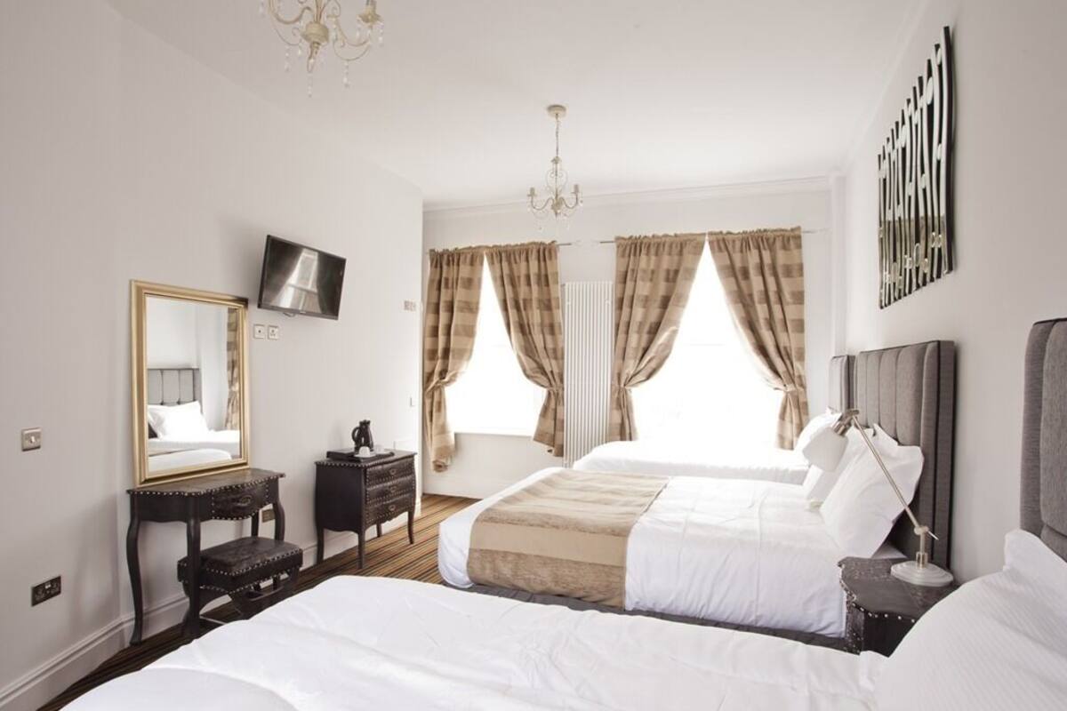 Ett hotellrum med två sängar, en platt-TV, en byrå, en spegel och en kristallkrona.
