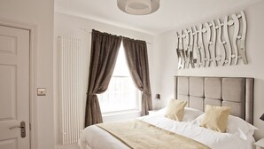 Habitación de hotel con una cama grande, un radiador, una ventana con cortinas y un aplique en la pared.