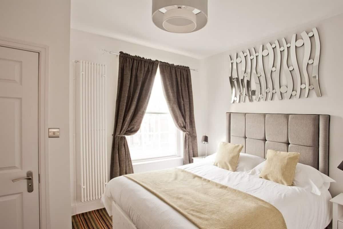 Ett hotellrum med en stor säng, ett element, ett fönster med gardiner och en väggmonterad lampa.