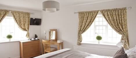 A bedroom with a bed, a desk, a chair, a television, and curtains.