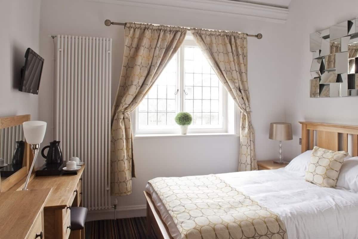Ett hotellrum med en säng, ett skrivbord med en lampa, ett element och ett fönster med gardiner.