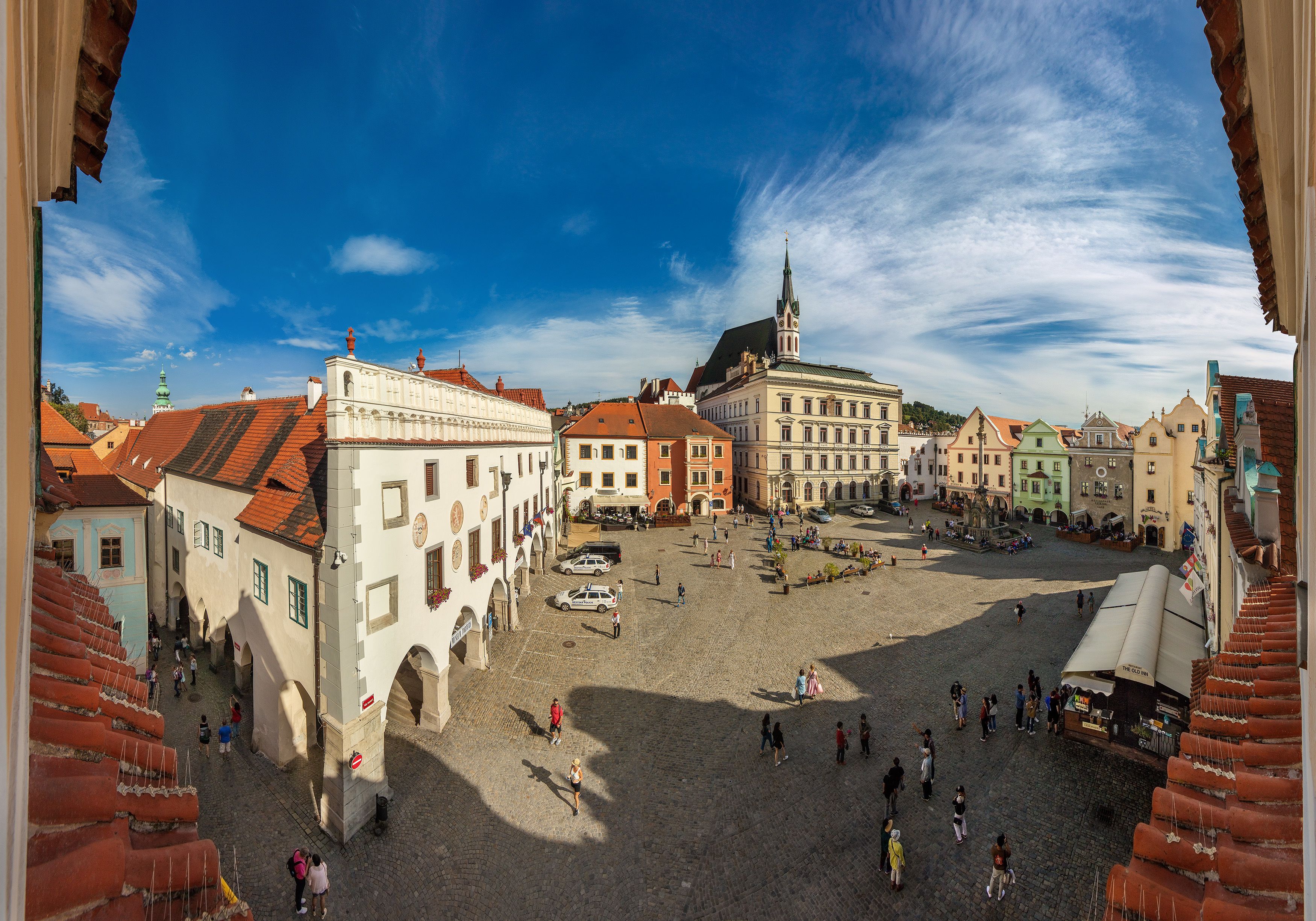 A cobblestone square with historic buildings, a church steeple, and a clear sky.