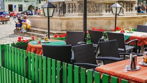 Outdoor seating with wicker chairs and tables, a statue in the background, and a fountain. - Hotel Zlaty Andel (Cesky Krumlov)