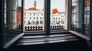 A view through a window with a metal frame, displaying a building with a clock tower and a red-roofed structure. - Hotel Zlaty Andel (Cesky Krumlov)