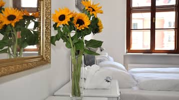 Habitación de hotel con cama, cómoda blanca, un jarrón con girasoles y un espejo con marco decorativo.