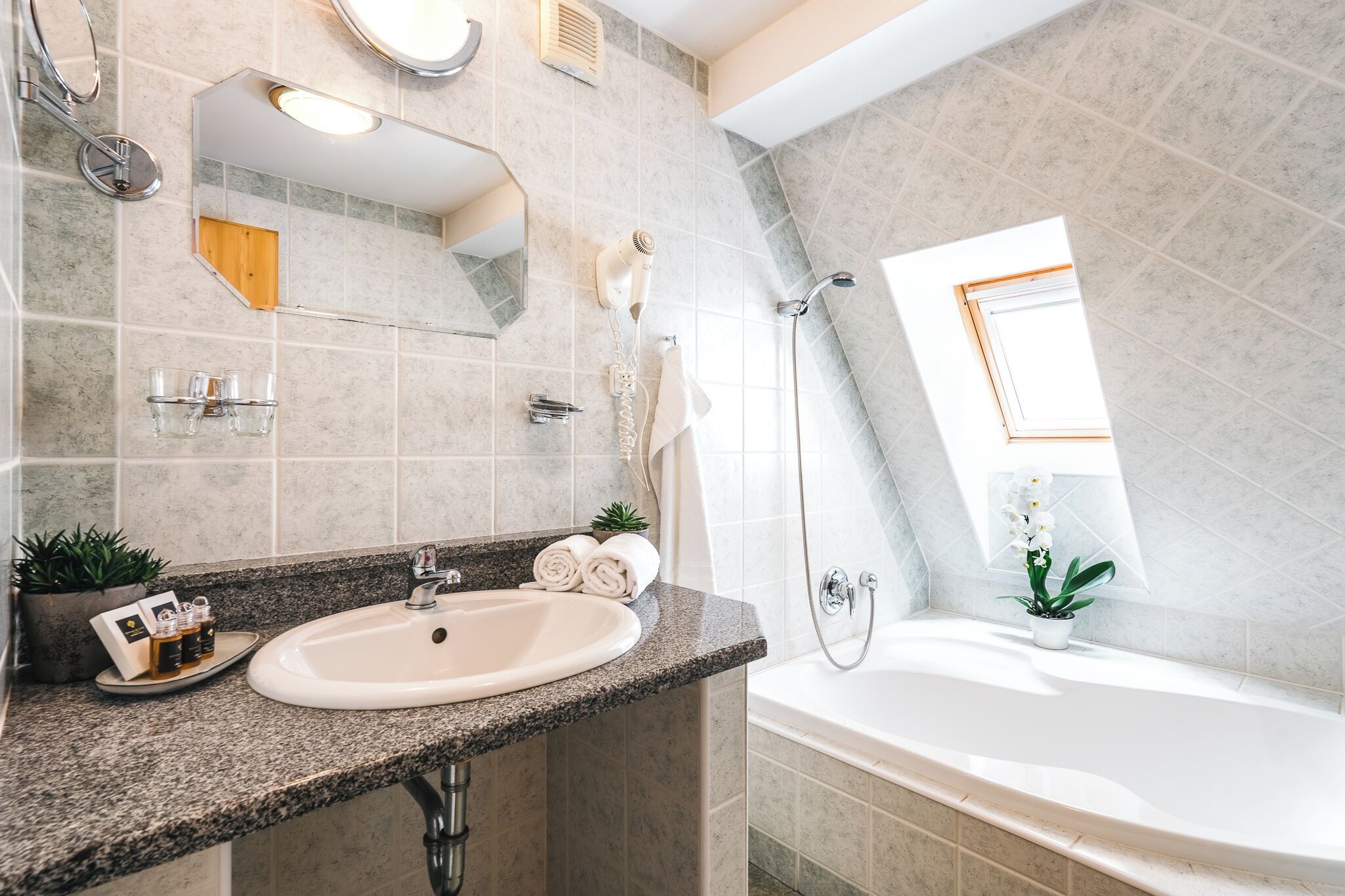 A modern bathroom with a granite countertop, a sink, a mirror, a shower, and a window.
