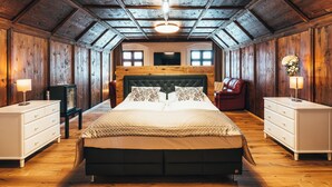 A bedroom with a large bed, wooden walls, a wooden ceiling, and a small table with a lamp. - Hotel Zlaty Andel (Cesky Krumlov)
