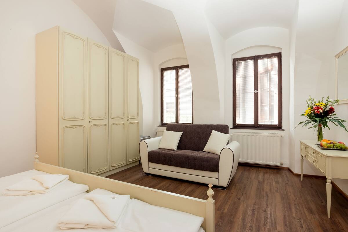 A bedroom with a bed, a sofa, a wardrobe, a radiator, and a window with blinds.