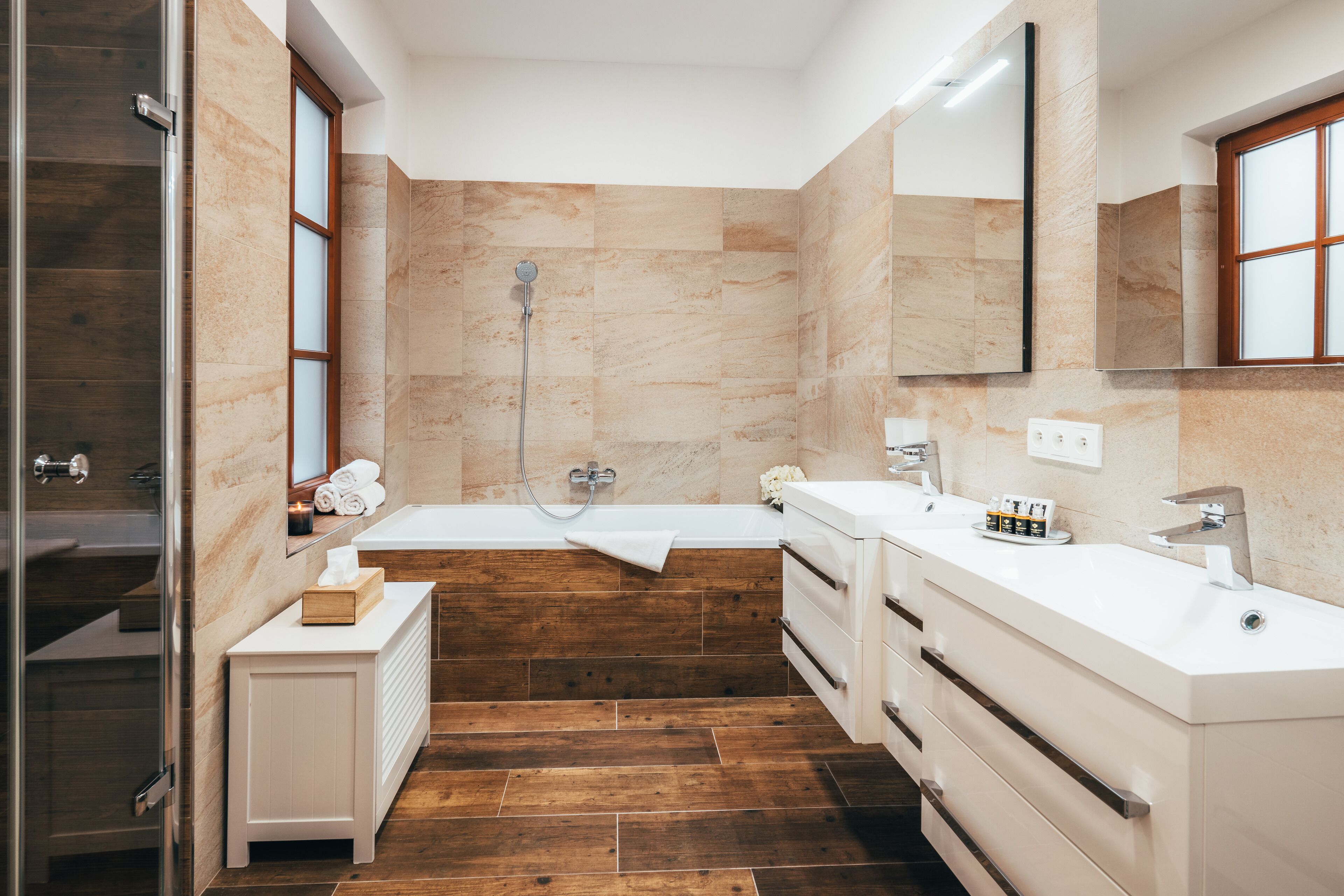 A modern bathroom with a shower, two sinks, a large mirror, and wooden flooring.