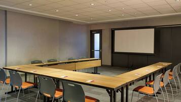 Sala de conferência com uma mesa comprida, cadeiras, tela de projetor e piso coberto de carpete.