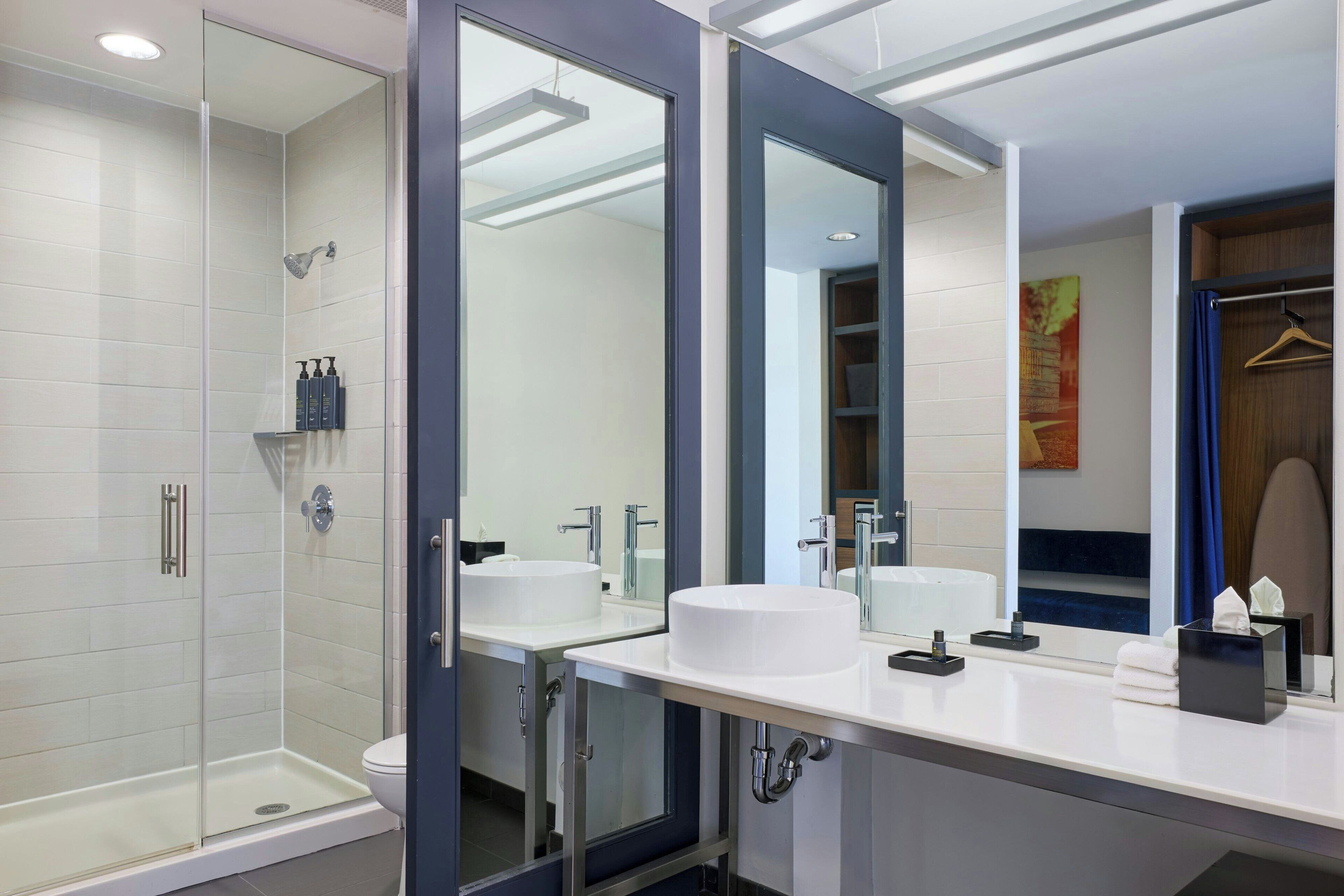 Un baño moderno con cabina de ducha de vidrio, dos lavamanos y un espejo grande.