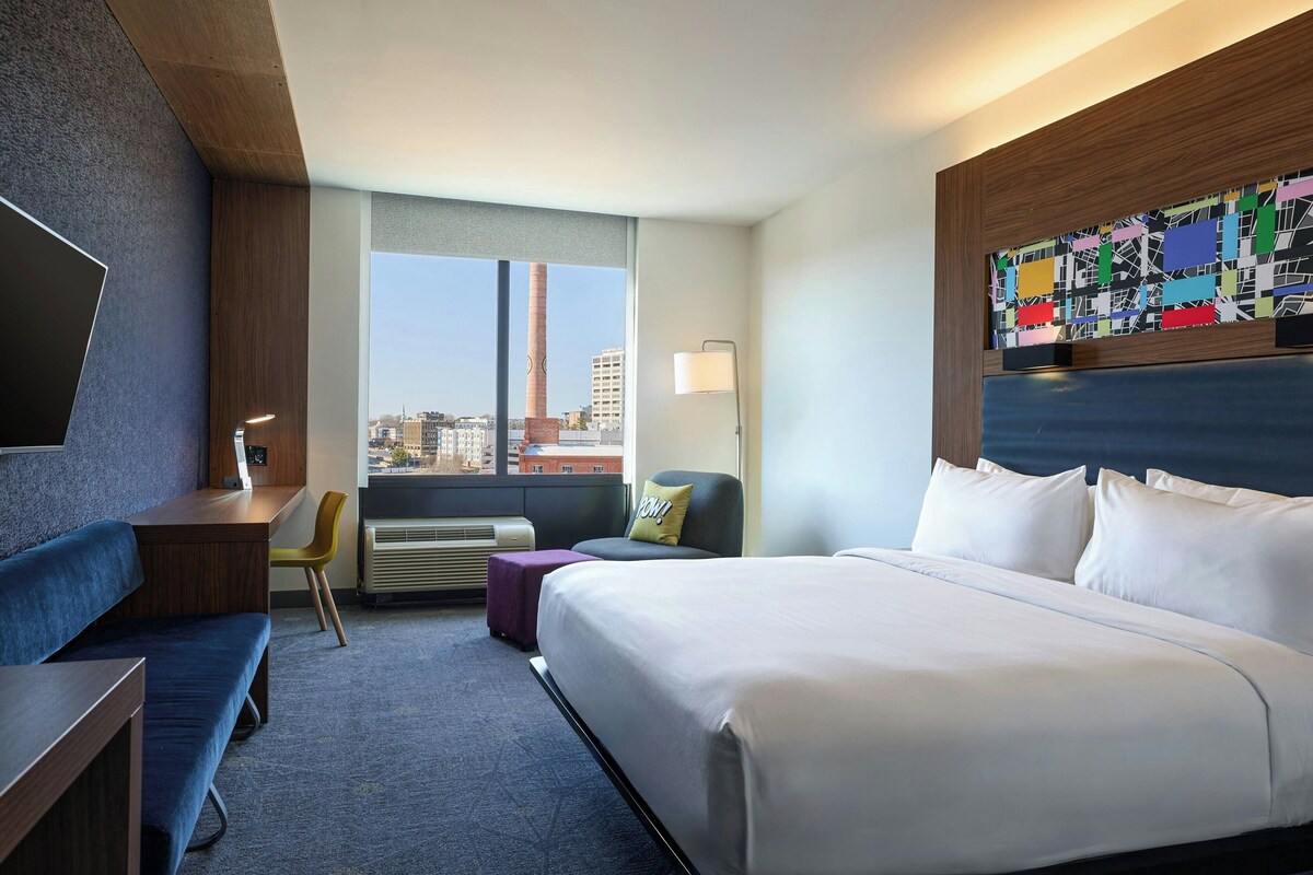 Habitación de hotel con una cama grande, un escritorio, una silla y vistas a la ciudad.