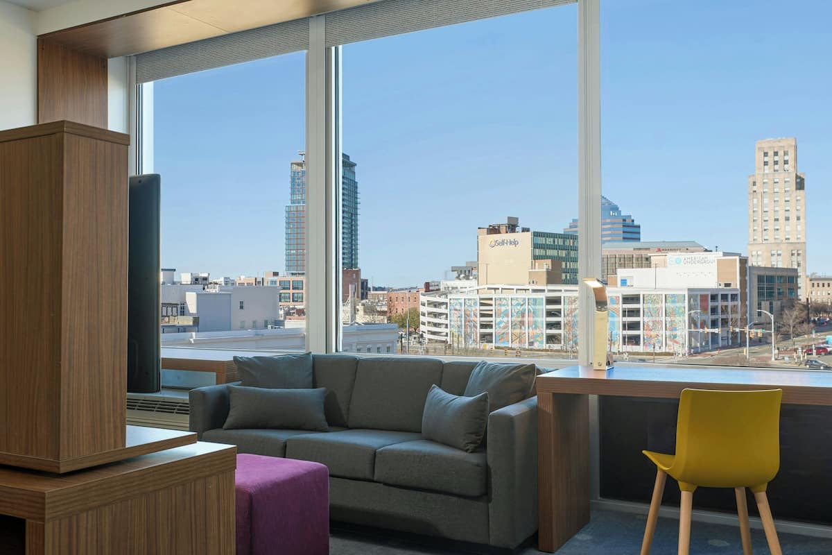 A modern room with a large window, a sofa, a yellow chair, and a wooden cabinet.