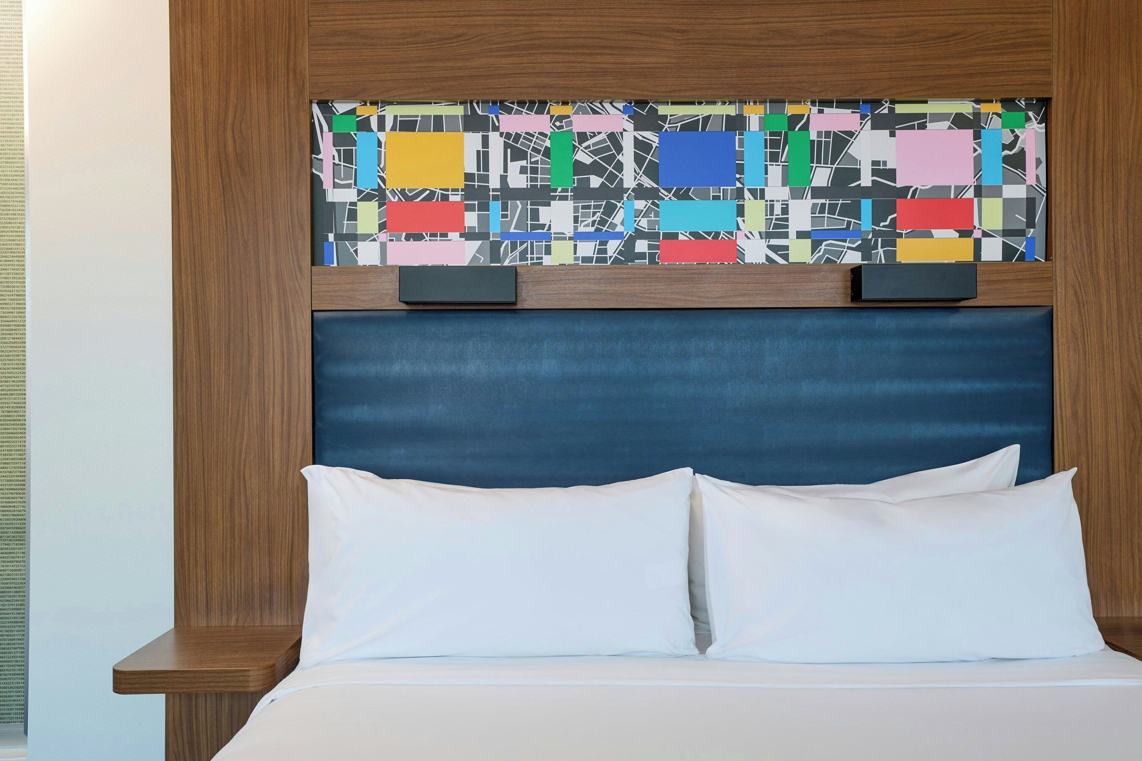 A bed with white linens and a blue headboard, flanked by wooden nightstands.