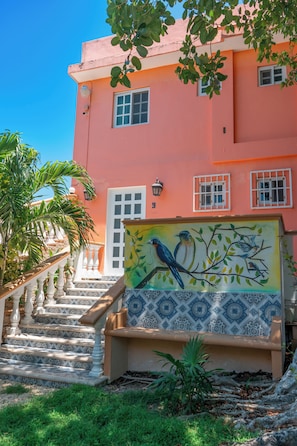 A multi-story building with a pink facade, a staircase with white balustrades, and a mural of birds on the lower wall. - Villa Pajaros (Isla Mujeres)