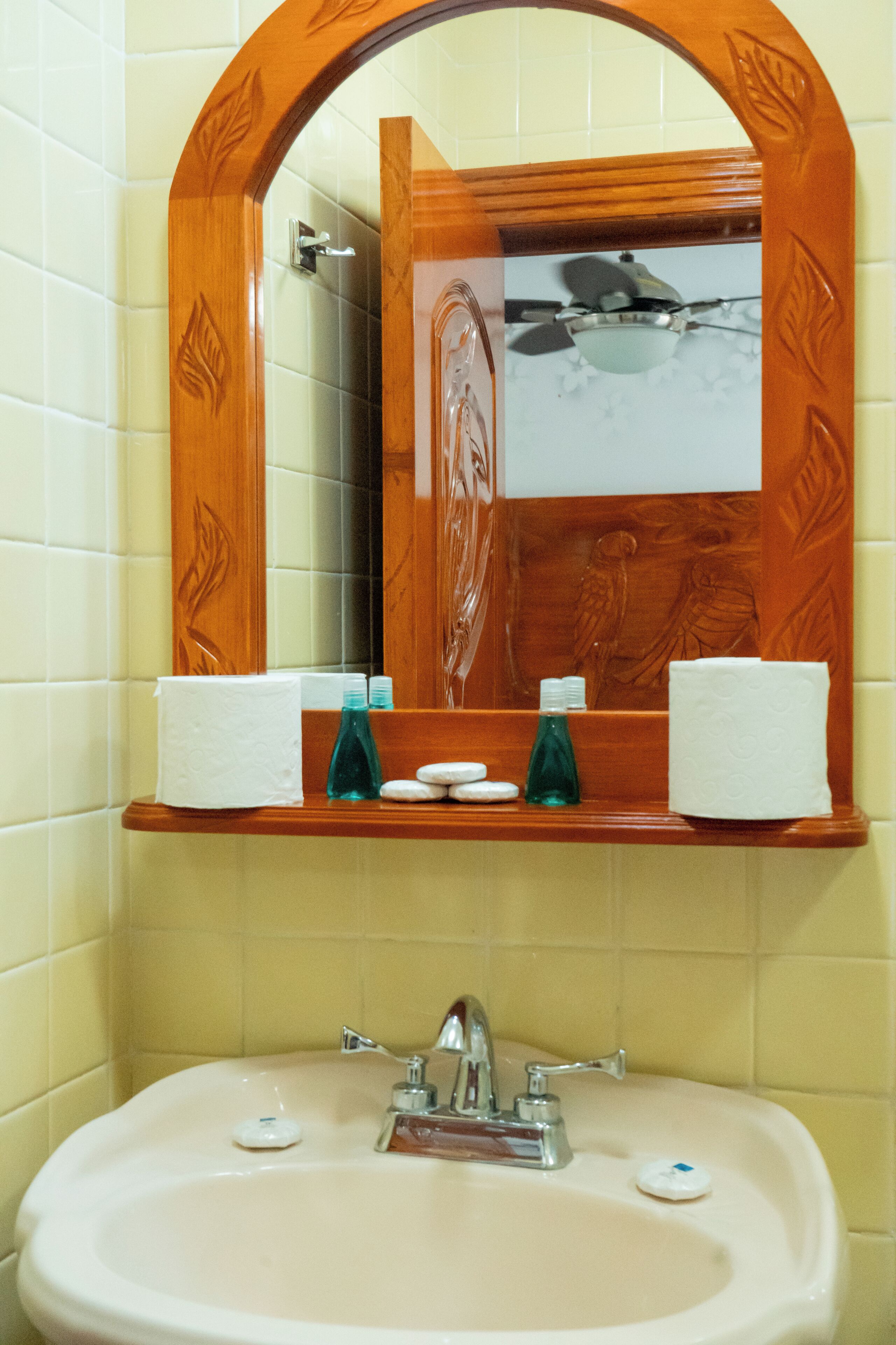 A bathroom with a wooden-framed mirror, a sink with a faucet, and a shelf with toiletries.
