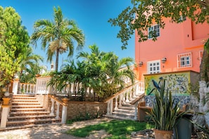 A staircase leading to a building with a colorful mural, surrounded by palm trees and greenery. - Villa Pajaros (Isla Mujeres)