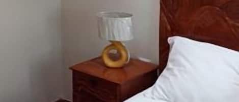 A hotel room with a wooden headboard, a bed with white bedding, a nightstand with a lamp, and a framed picture on the wall.