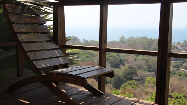 A wooden deck with a bench and a view of a forested landscape through large windows.