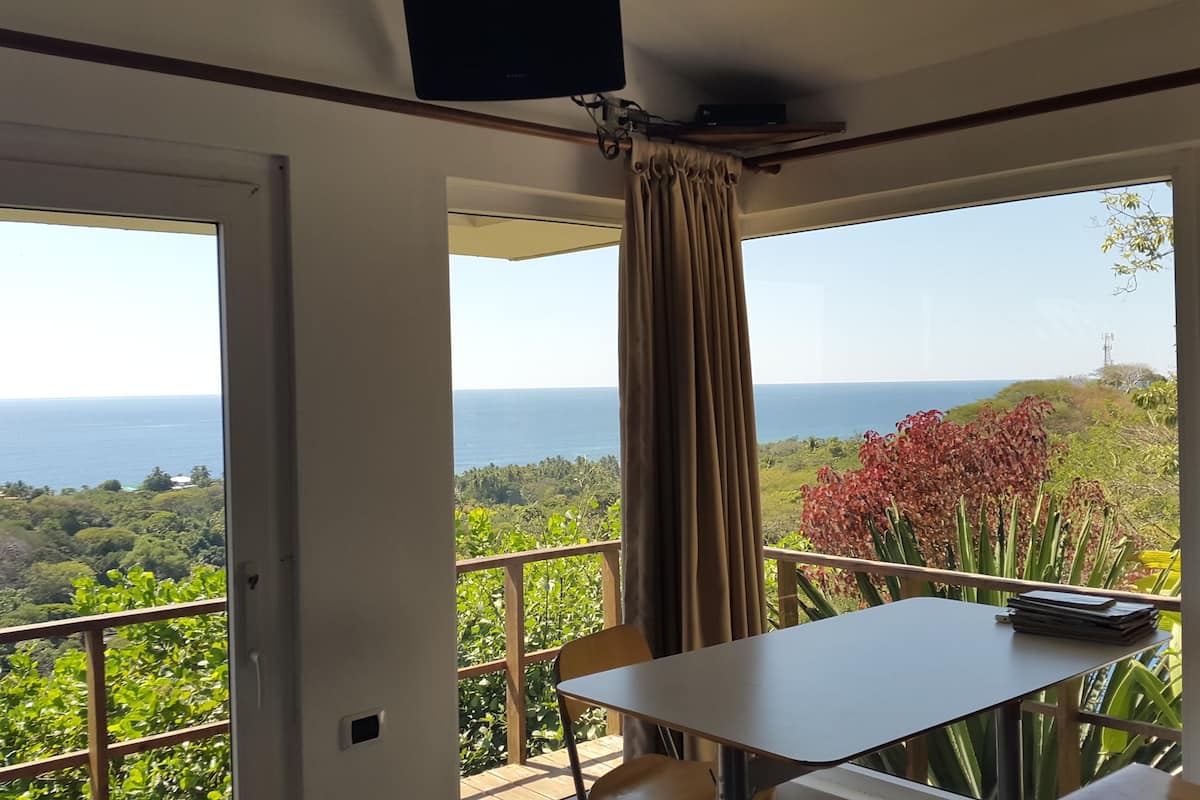 A balcony with a table and chairs, overlooking a scenic view of the sea and greenery.