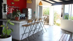 A kitchen with a red wall, a bar area with stools, a refrigerator, and a potted plant.