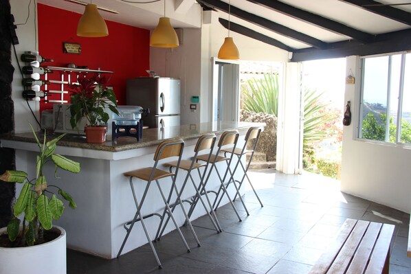 A kitchen with a red wall, a bar area with stools, a refrigerator, and a potted plant.