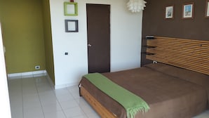 A bedroom with a wooden bed, a green throw blanket, a door, and a wall-mounted light fixture.