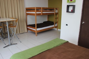 A bunk bed with a desk and chairs, a green mat, and a brown bedspread.