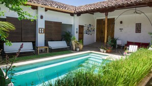 Un área junto a la piscina con techo de baldosas, un banco y plantas en macetas.