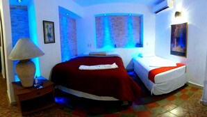Habitación de hotel con una cama grande, una cama más pequeña, una mesita de noche, una lámpara y un aire acondicionado de pared.