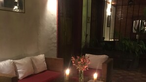 Un área de descanso tenuemente iluminada con muebles de mimbre, un sofá rojo y un florero con flores.