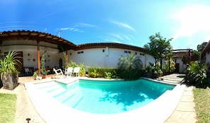 Una piscina con borde de baldosas, rodeada de plantas en macetas y mobiliario exterior.