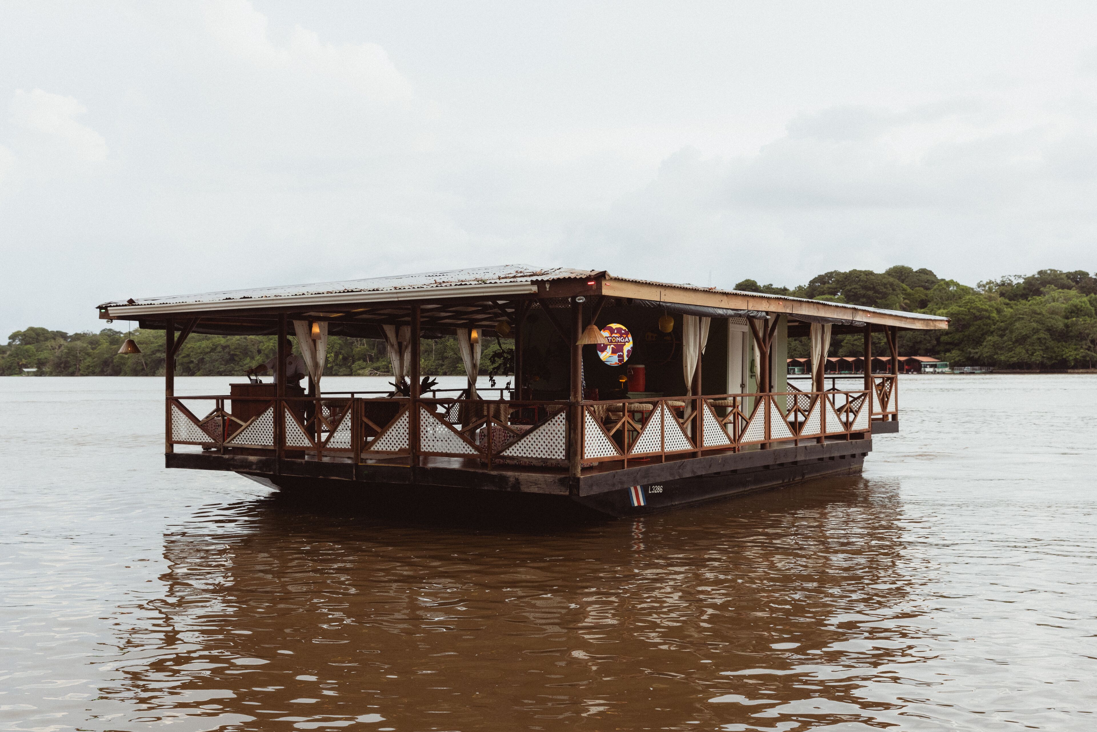 A stationary boat with a covered deck and railings, floating on a body of water.