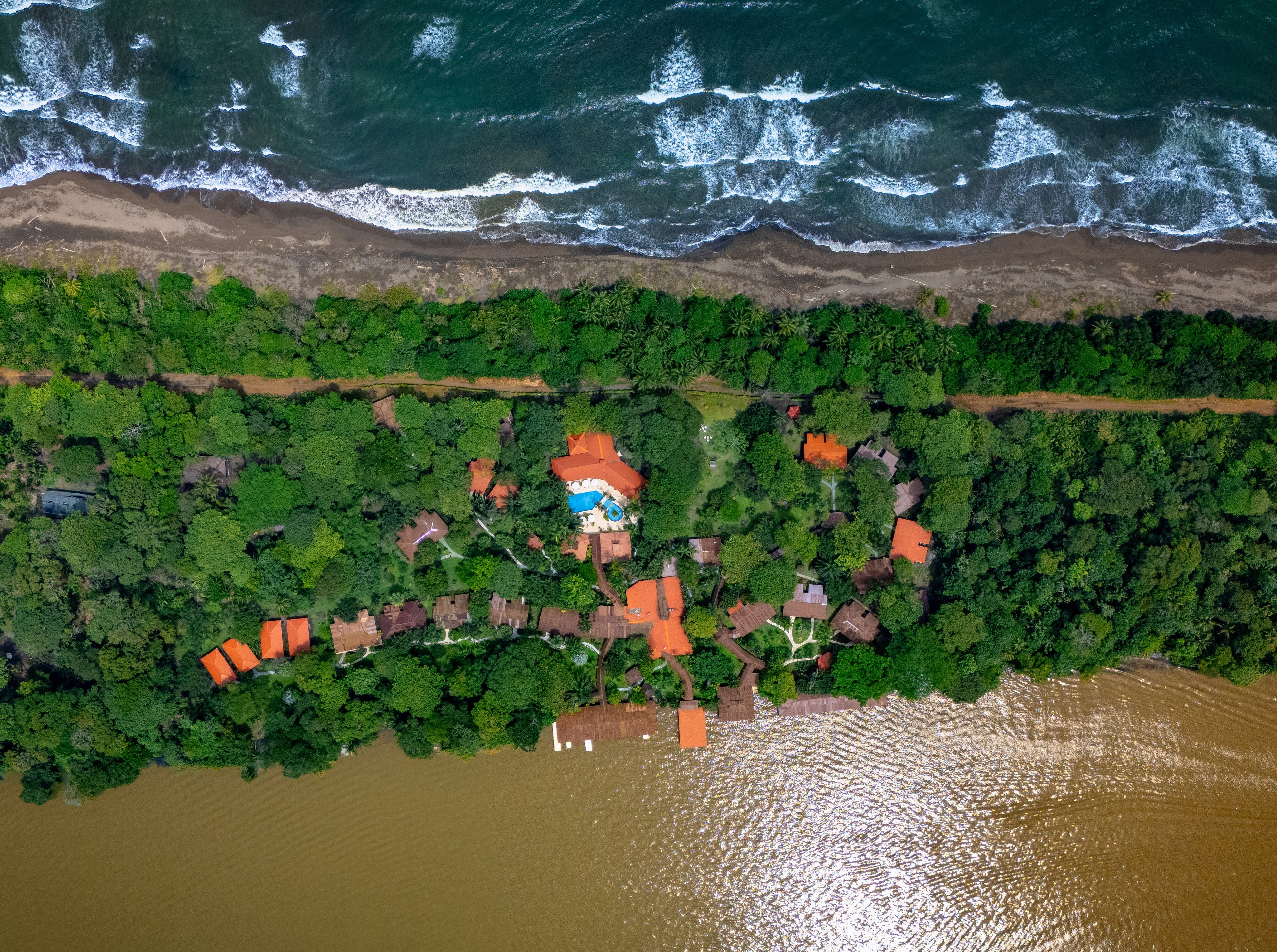 Vista aérea de una propiedad costera con piscina, rodeada de abundante vegetación y una playa arenosa.