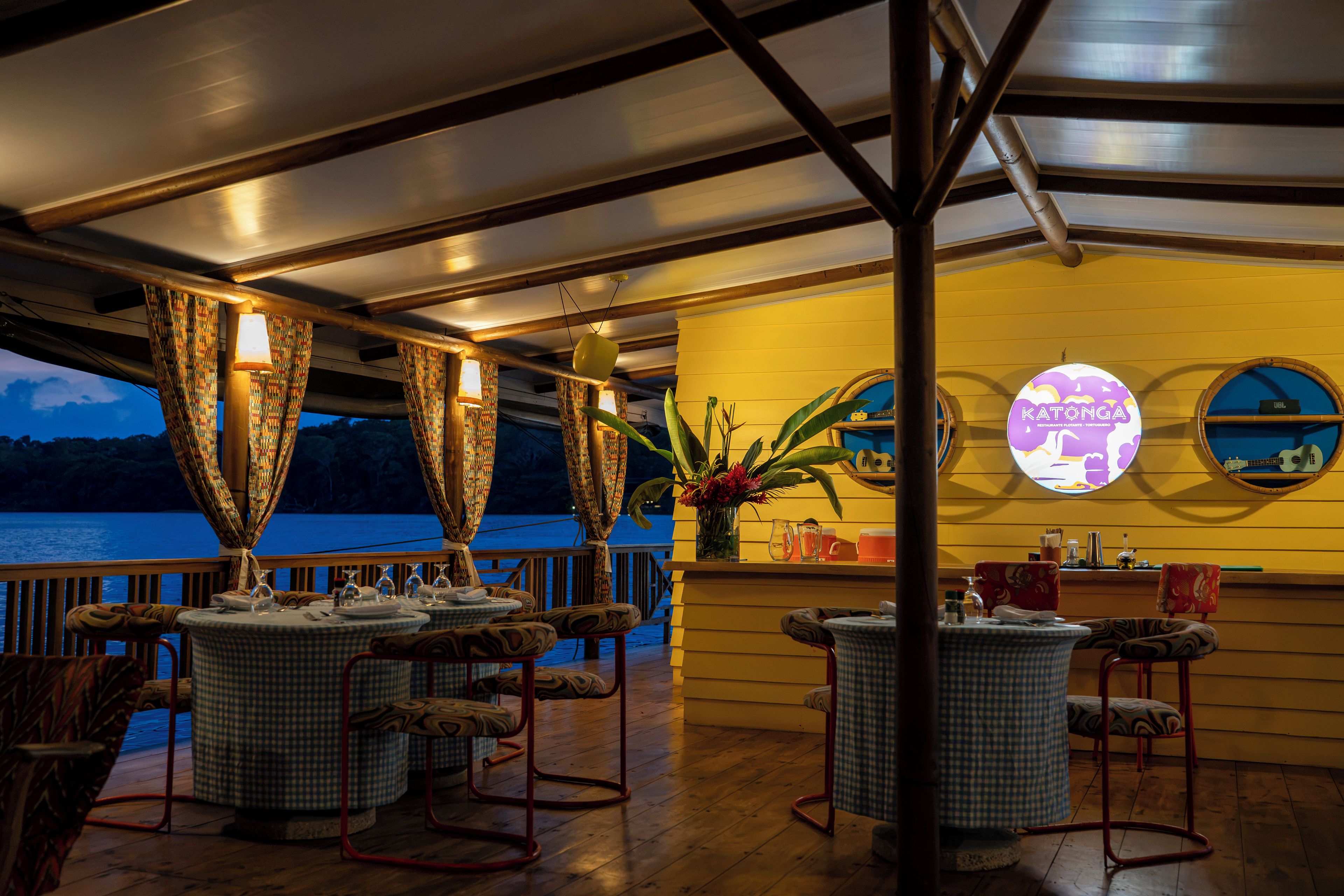 A restaurant with tables and chairs, a view of the sea, and a sign that reads 'Katonga.'