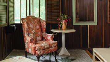 Una habitación con un sillón estampado con motivos florales, una mesita redonda con un jarrón y un banco.